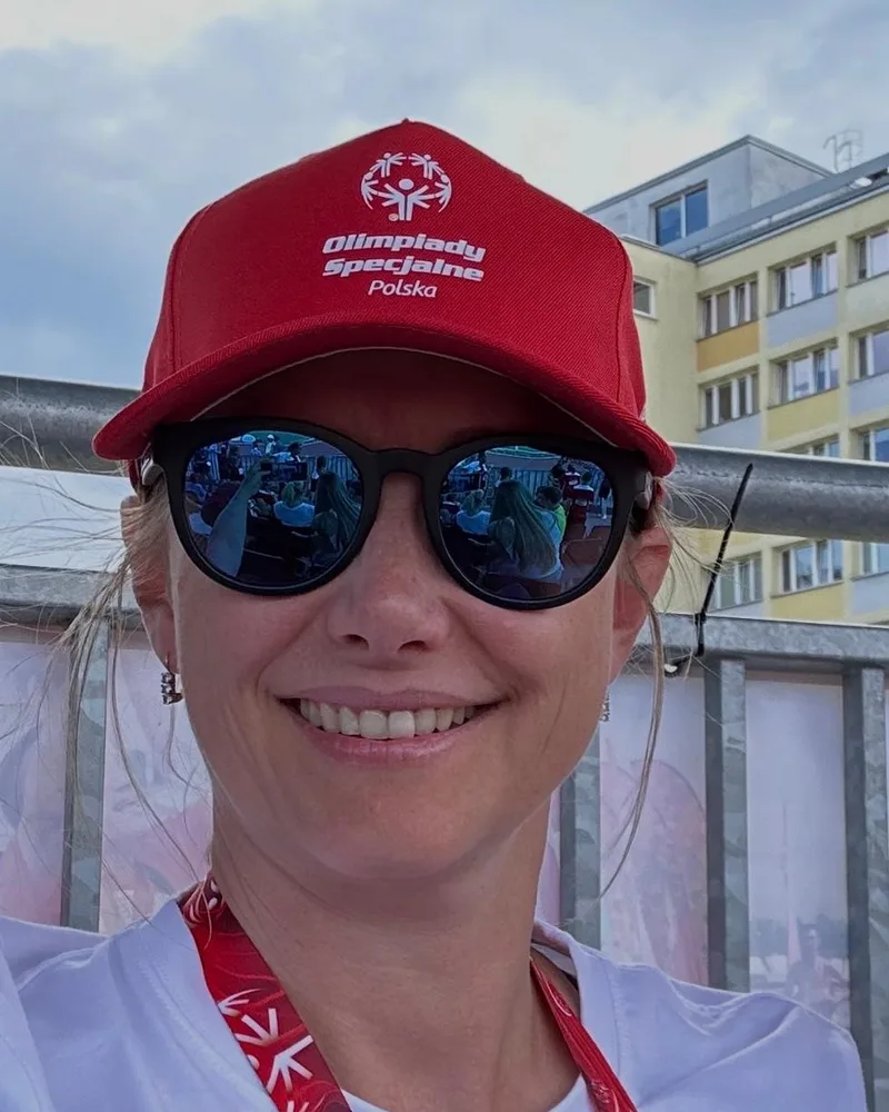 Uśmiechnięta Beata Dąbrowska w czapce Olimpiad Specjalnych Polska